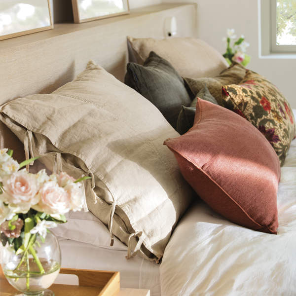dormitorio con cabezal de obra, cojines con ropa de cama de lino, color morado, verde y flores